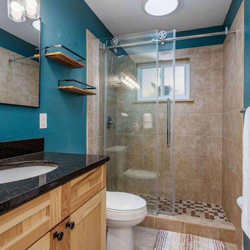 - stylish bathroom with teal accent walls and a spacious glass walk in shower
- natural wood vanity with granite countertop and sleek black fixtures
- modern lighting, floating shelves, and tiled shower floor add a designer touch