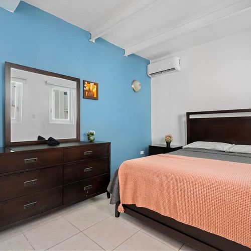 Unwind in the comfort of a cozy and well-lit room, where a plush bed adorned with a stylish coral blanket invites relaxation, set against the backdrop of a vibrant blue accent wall.