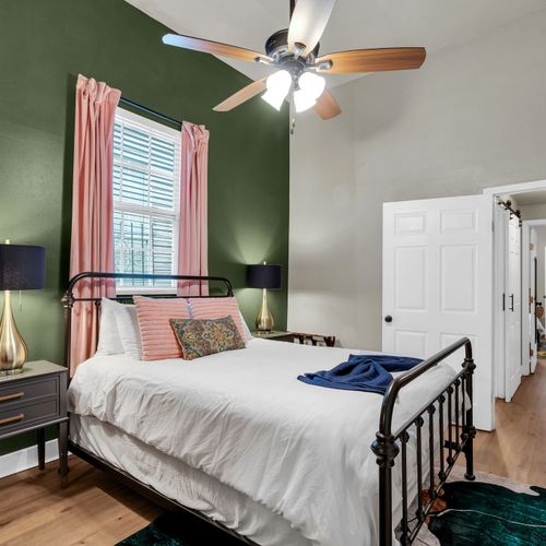 Airy bedroom w/ green walls, a ceiling fan & natural light streaming in.