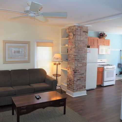 Living room: the apartment has a cozy living room with a sofa, chair, ceiling fan, and live streaming television.