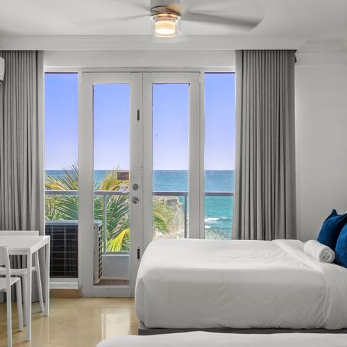 Indulge in the ultimate seaside escape in this spacious bedroom, offering two plush beds and floor-to-ceiling glass doors that open to stunning panoramic ocean vistas.
