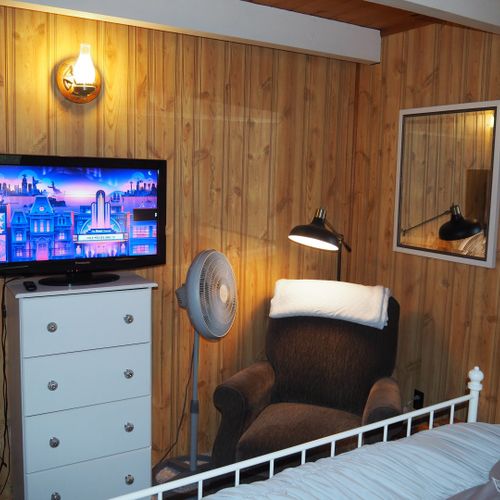 Bedroom #1 (main floor):  features a queen-size bed, chair, dresser, nightstands with lamps, fan, floor lamp, and its own television.
