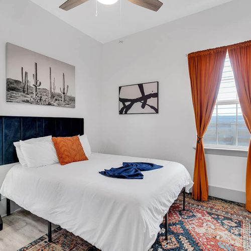 Bright bedroom w/ crisp white walls, teal curtains, & a bold orange headboard.