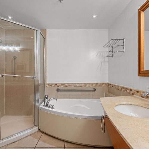 Unwind in the beautifully designed bathroom, featuring a refreshing glass-enclosed shower and a separate, inviting bathtub, perfect for a soothing soak.