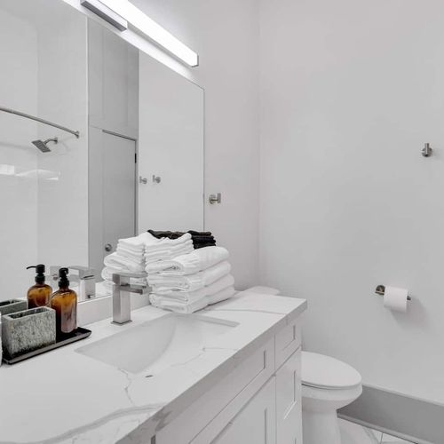 Modern bathroom w/ marble vanity, tub & shower combo, & neatly folded towels.