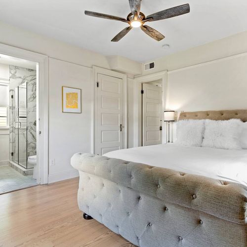 Soft, airy bedroom w/ natural light pouring in through large windows.