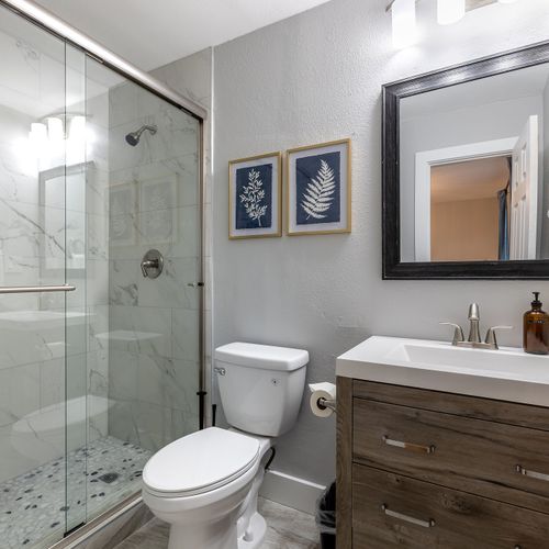 Recently refinished bathroom features a tub/shower option with floor to ceiling marble-styled tile and a large rustic vanity.