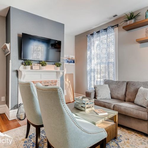 - stylish living room with mounted tv, white fireplace mantel, and cozy neutral sofa for relaxation
- blue accent chairs and layered rugs add charm and comfort to this welcoming space
- sunlight filters through patterned curtains and floating shelves