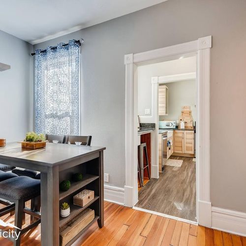 - compact dining space features a tall table with bench and chairs for group meals
- stylish shelving and a patterned curtain add warmth to the neutral palette
- easy access to the kitchen through a classic framed doorway