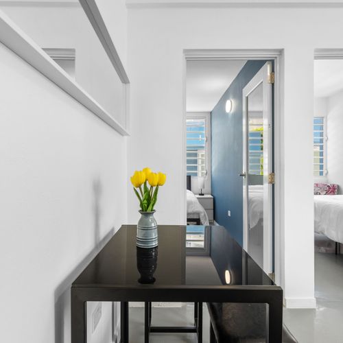 Capture a side perspective of two bedrooms, both featuring a stylish black table adorned with a burst of vibrant color from a bouquet of yellow flowers.