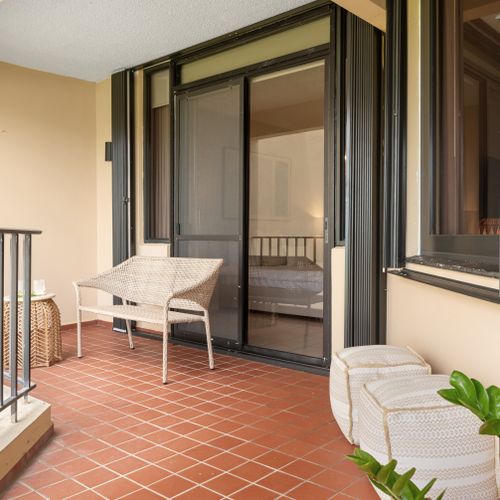 Relax in comfort outdoors! This charming balcony offers a peaceful retreat with views of lush greenery and distant sea.
