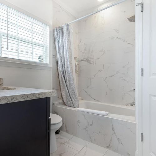 Private ensuite bath w/ marble-finish walls & a toilet — shower just off to the right.