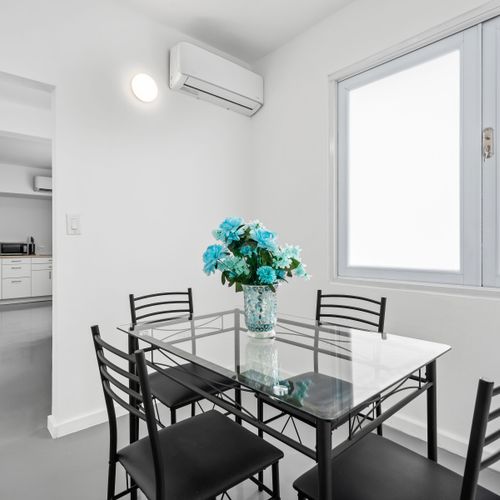 Indulge in urban elegance with our modern dining space, complete with a sleek glass table, chic black chairs, and a vibrant blue floral centerpiece.