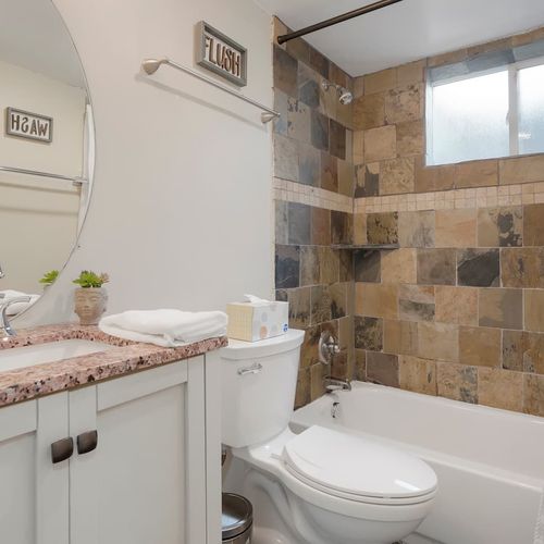 - stylish bathroom featuring rustic tile shower, granite counter, and round mirror
- soft lighting, fun signage, and thoughtful touches add charm to the space
- clean, cozy, and complete with all the essentials for your stay