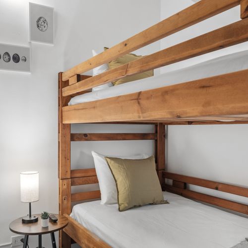 Step into a cozy haven with our modern bunk bed room, featuring clean white linens and a chic bedside lamp.