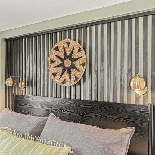 Cozy textured pillows & a plush striped throw that invites you to unwind - statement headboard with bold black slats & tribal wall art adds depth & design flair - warm brass sconces provide soft lighting for your nighttime reads