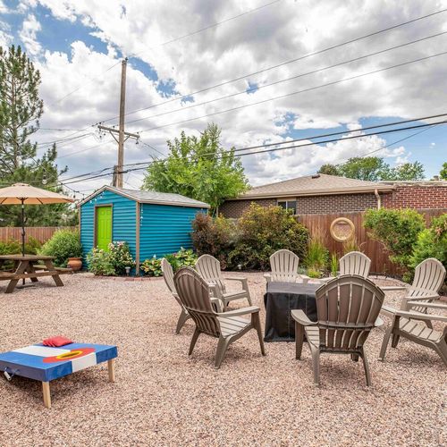 - spacious backyard setup with fire pit seating, string lights, and greenery
- enjoy friendly competition with cornhole boards or relax under the picnic umbrella
- bright blue shed and gravel patio add charm and vibrant character to the space