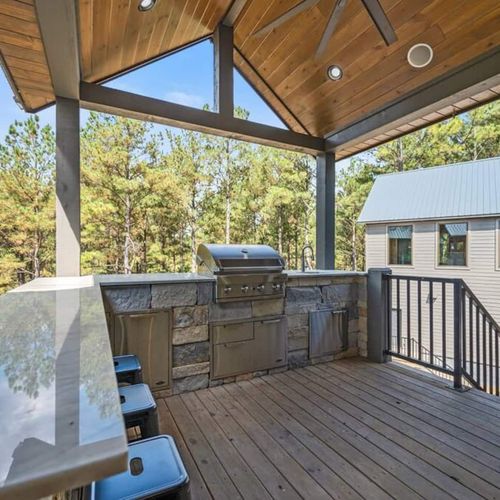 Outdoor kitchen with gas grill, bar top seating and mini fridge.