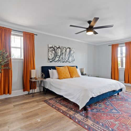 Bright master bedroom w/ bold orange curtains, attached bathroom & comfortable bed.