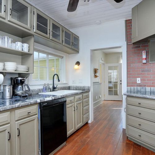 - well equipped kitchen with open shelving, dishes, and a full suite of appliances
- earth toned cabinets, exposed brick backsplash, and wood floors add character
- bright and functional layout ideal for meal prep and morning coffee routines