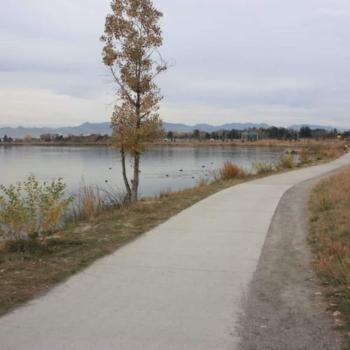 A peaceful lakeside trail curves gently beneath overcast skies, lined with dry autumn grass.
