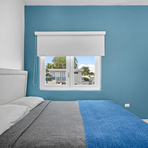 Experience relaxation in a minimalist space that combines comfort with clean lines and features a cozy bed, highlighted by a striking blue wall for a pop of color.