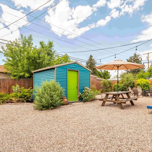 - spacious and cheerful backyard featuring a bright blue shed with a lime green door
- extra seating with a picnic table and fire pit area surrounded by greenery
- cornhole game setup and string lights promise all day outdoor entertainment