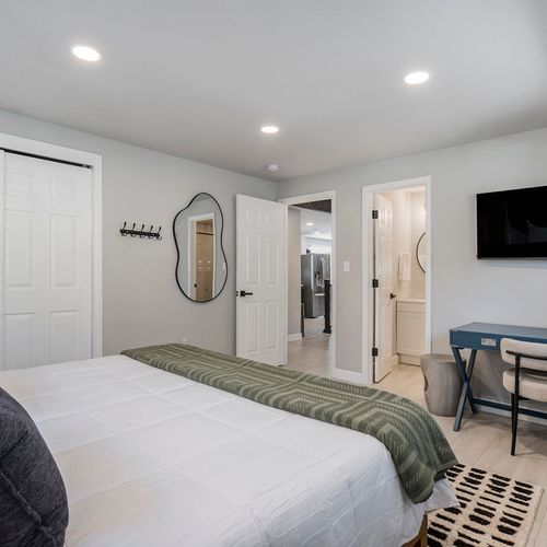This serene primary bedroom complete with a convenient desk for productivity, a flat-screen tv for entertainment, and an entrance to the ensuite bathroom, offering both comfort and functionality for your stay.