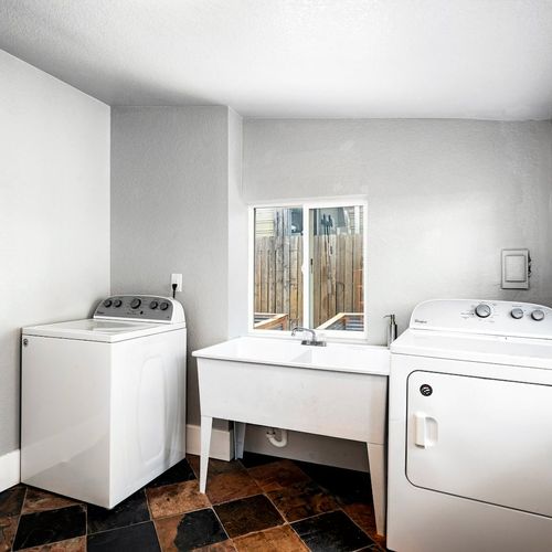 - functional laundry space featuring side by side washer and dryer setup
- deep wash basin and tiled floors offer practicality in a clean design
- natural light from the wide window makes this chore friendly zone inviting
