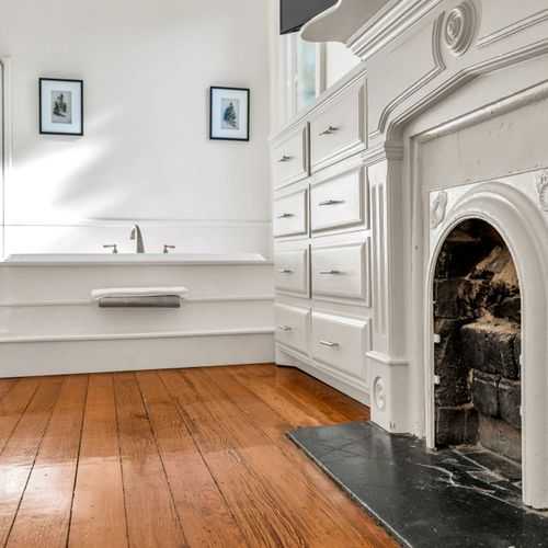 Elegant bathroom with a restored fireplace detail, a spacious soaking tub, and classic wood flooring for a touch of timeless charm.