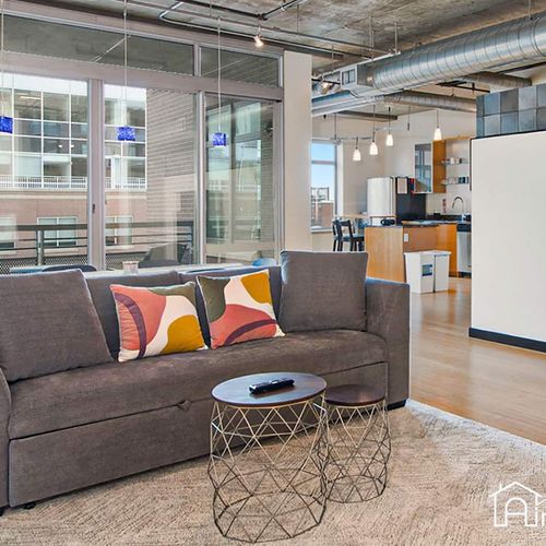 - lounge in an airy industrial-style space featuring a comfy sofa and playful accent pillows
- floor to ceiling windows let in bright city light while offering privacy and views
- sleek furniture and exposed ductwork create a modern downtown vibe