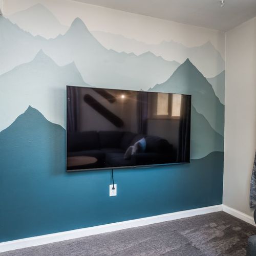 - wall mounted flat screen tv sits in front of a hand painted mountain mural
- muted tones of blue and gray create a calming artistic vibe in the space
- perfect for relaxing with your favorite shows in a cozy serene corner