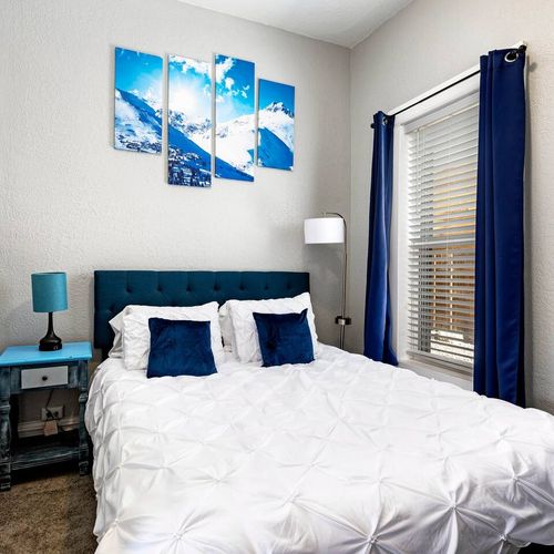 - stylish bedroom with blue accents, teal headboard, and bold mountain artwork
- crisp white bedding and blackout curtains promise restful, undisturbed sleep
- includes a nightstand, reading light, and natural light from large windows
