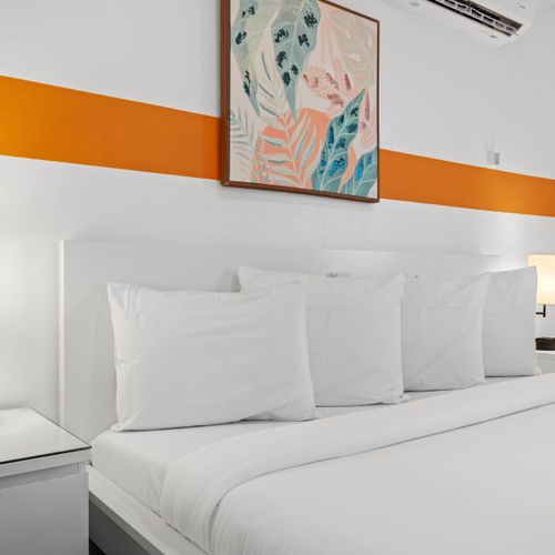 Drift off to sleep in our serene bedroom featuring a plush king-sized bed, accented with a vibrant orange stripe and complemented by a chic bedside lamp and nightstand for your convenience.