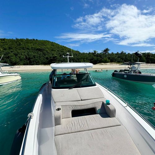 Picturesque harbor views: a classic wooden pier, gleaming boats, and lush green hills under a bright blue sky.