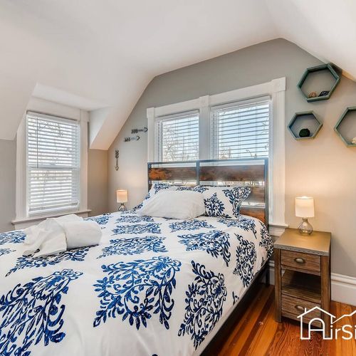 - welcoming bedroom with angled ceilings and a plush full size bed with crisp linens
- blue botanical design adds style while natural light filters through double windows
- nightstands with lamps and modern honeycomb shelves enhance the charm