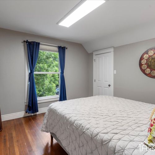 The third bedroom offers a queen bed and soothing natural colors, enhanced by abundant natural light streaming through a large window.