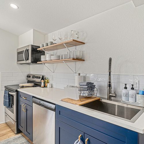 - enjoy cooking in this sleek setup with stainless steel appliances and deep farmhouse sink
- open shelves keep glassware and dishes within easy reach for every meal
- navy blue cabinetry and white tile backsplash add bold modern charm