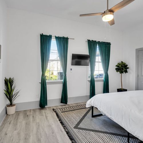 Bright bedroom w/ teal drapes, a/c unit, & a lush plant for a fresh, airy feel.