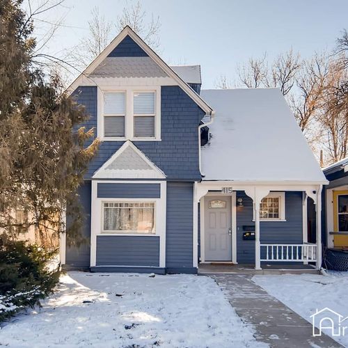 Classic blue victorian style home with crisp white accents, set against a peaceful snow covered yard.