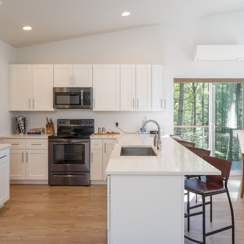 A fully equipped chef's kitchen — quartz island, stainless appliances, and a forest view while you cook.