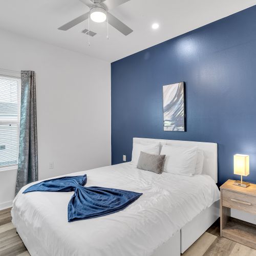 Rest easy in this cozy bedroom with a calming blue accent wall, soft lighting, and inviting linens that make relaxation effortless.