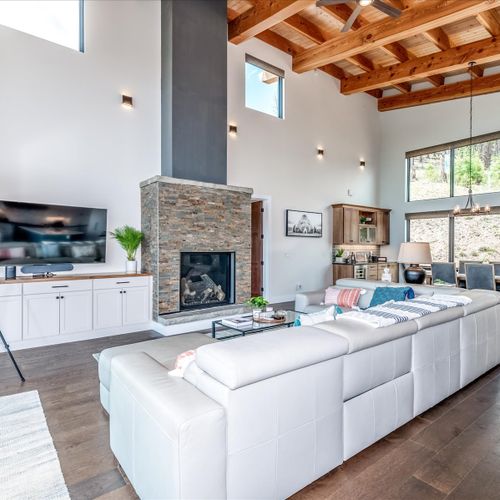 Living room with beamed-lined, vaulted ceilings, well-appointed furnishings, and infinite floor-to-ceiling windows.