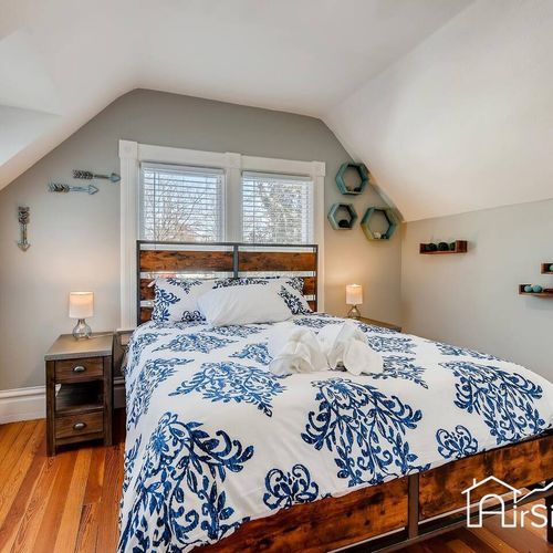 - cozy bedroom with rustic wood headboard & bold blue patterned bedding for a fresh coastal feel
- twin windows bring in natural light while bedside lamps create a soft evening glow
- decorative wall art & hardwood floors complete the inviting space