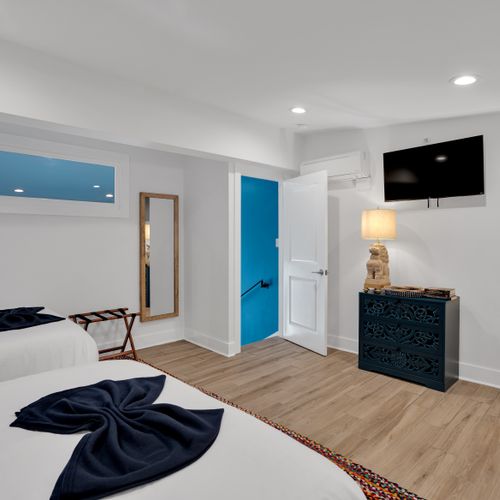 Bedroom 2 w/ a teal door, wall-mounted TV & warm wood floors for a cozy retreat.
