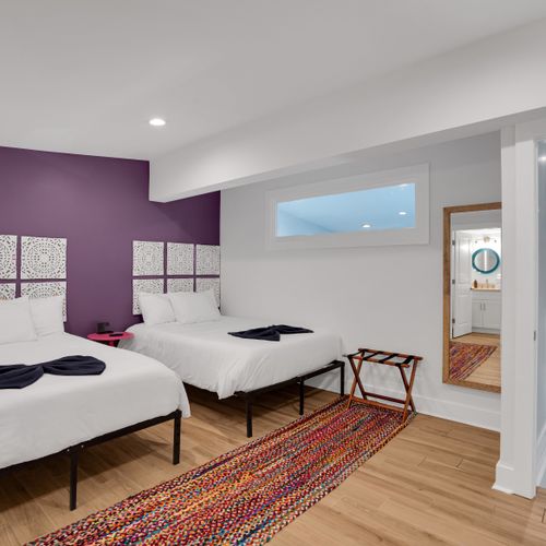 Bedroom 2 w/ twin beds, bold purple wall & a patterned rug for eclectic charm.