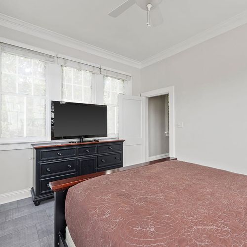 Relax in this cozy bedroom featuring a plush bed, ample natural light, and a flat-screen TV for your entertainment. Perfect for unwinding after a day exploring the vibrant streets of New Orleans.