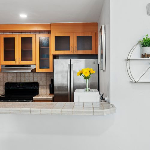 Bright kitchen area with electric stove, microwave hood, and a coffee machine, connecting to a hallway with a blue accent wall.