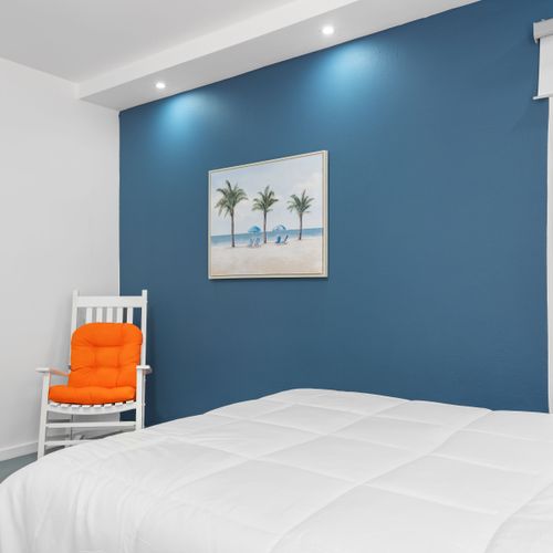 Relax in this well-appointed bedroom featuring a calming blue color scheme, modern artwork, and cozy seating. The room’s contemporary design elements and spacious bed offer a harmonious blend of modern aesthetics and comfort.