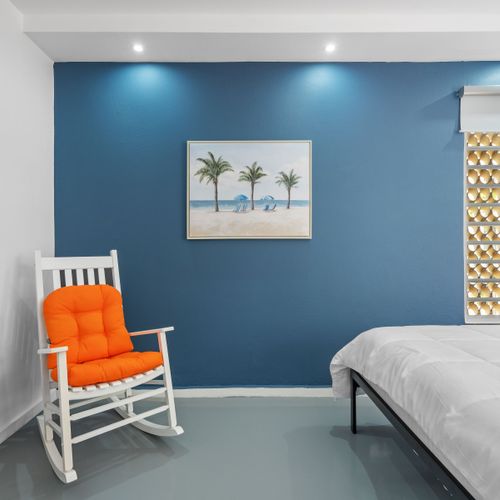 Enjoy a cozy, modern room with a bold blue accent wall, comfortable white rocking chairs, and contemporary decor, creating a vibrant yet relaxing space.